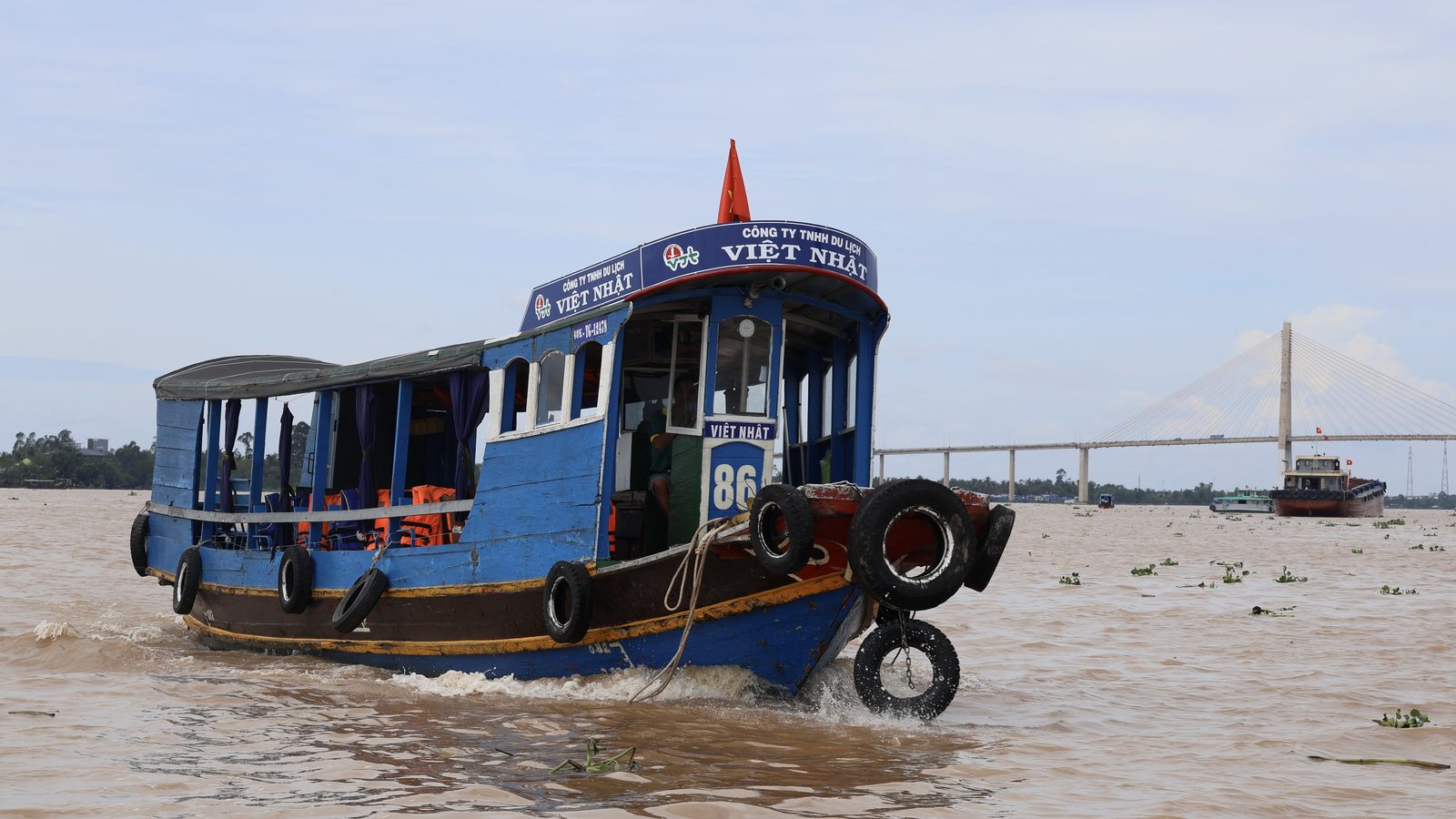 Blue river boat on the Mekong at My Tho with a cable-stayed bridge behind